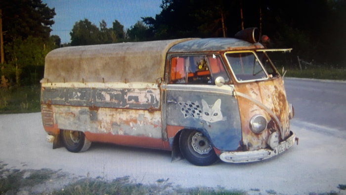 Gammal pick-up med sliten lack, rost och kattdekal, parkerad vid vägkanten.