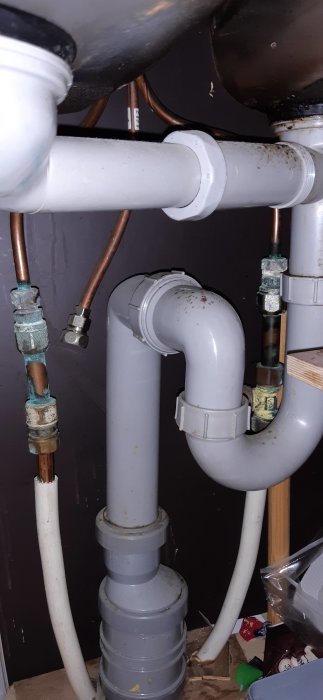 Gammal vvs-installation med koppar- och plastledningar under diskbänk.