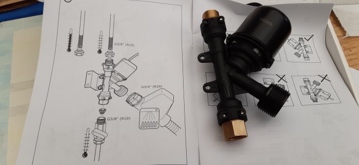 Monteringsinstruktioner för rörkopplingar och ett svart elektriskt avstängningsventil vid sidan av på ett bord.