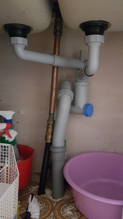 Underdiskbänksvy med rörkopplingar och vattenlås, potentiell avloppsproblematik i en sommarstuga.