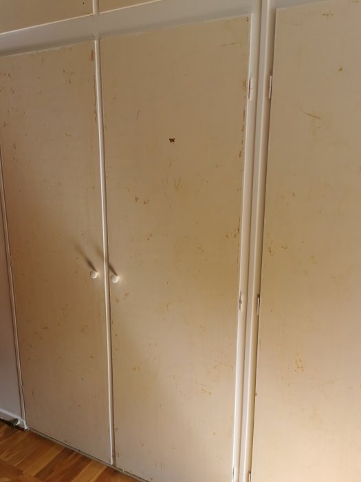 Slitna vita inbyggda garderobsdörrar från 50-talet i ett sovrum, redo för renovering och ommålning.