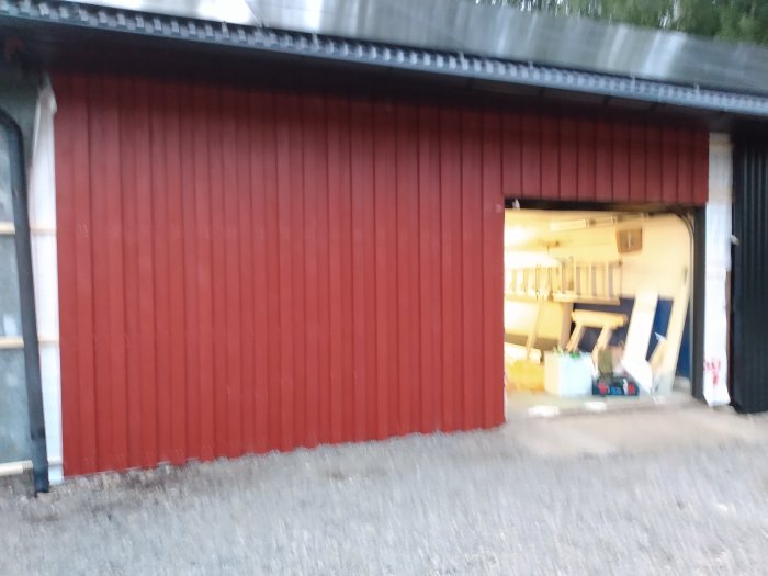 Halvöppen garageport med inblick till verkstadsutrymme, kvällsljus, suddig bild.