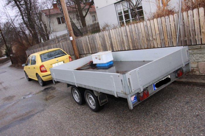 Gul personbil parkerad framför ett grått tvåaxlat släp på en våt gata.