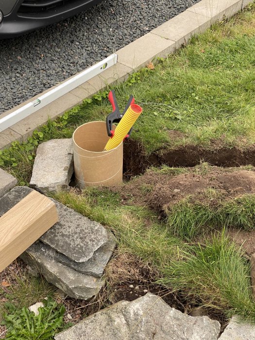 Installation av laddbox, grävd grop och ekstolpe med elledningar, intill stenläggning och gräs.