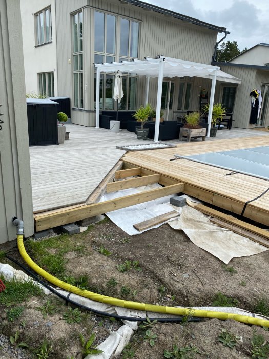 Pågående trallbyggnadsprojekt vid hus med befintligt däck och pergola, inklusive framställning av träreglar.