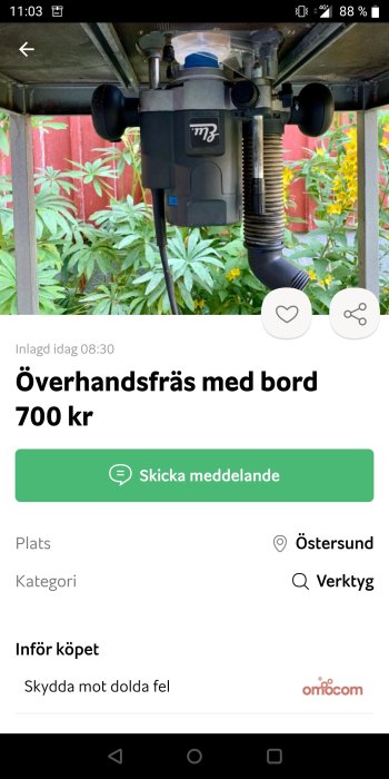 Överhandsfräs monterad på ett bord med bakgrund av växtlighet.