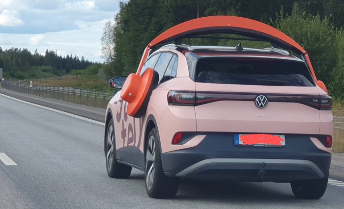 Rosa Volkswagen ID.4 elbil med orange takbox fastspänd på vägen.