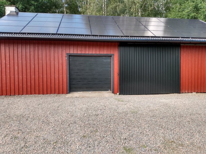 Röd träfasad med svart garageport och solpaneler på taket av en byggnad.