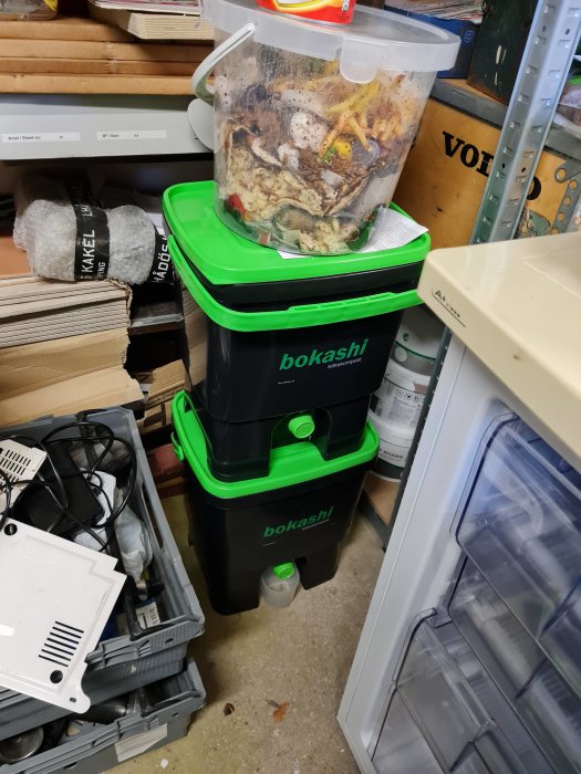 Bokashi-kompostbehållare och matavfall i ett trångt förrådsutrymme.
