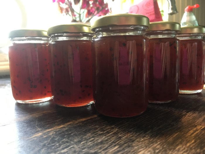 Burkar med hemgjord röd krusbärsmarmelad med chilitwist på ett bord.