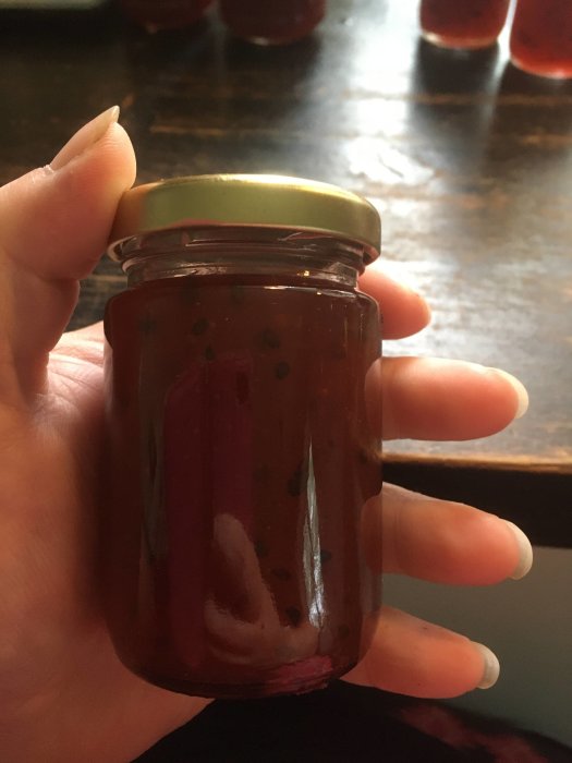 Hand håller en liten glasburk fylld med rödaktig krusbärsmarmelad och chilitwist.