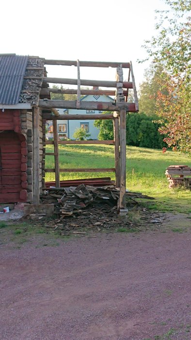 Delvis nedriven gammal vedbod med hoprörd bråte och överbliven stomme utomhus.