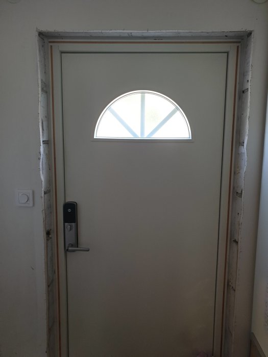 Nyinstallerad ytterdörr med färdigfrästa spår för smyg och halvrunt fönster ovanför.