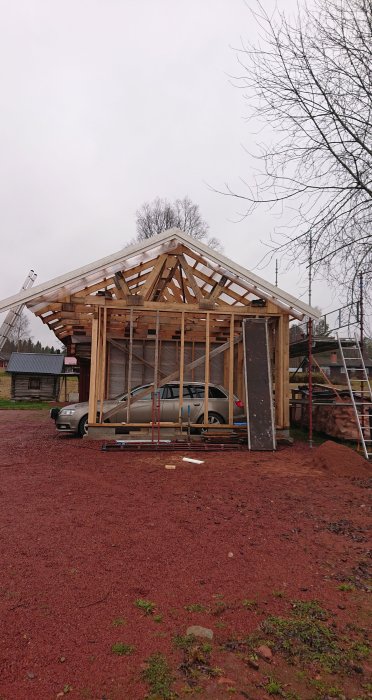 Högbyggt trästomme till carport med trampsäker kondensväv, timmerpanel och parkerad bil inuti.