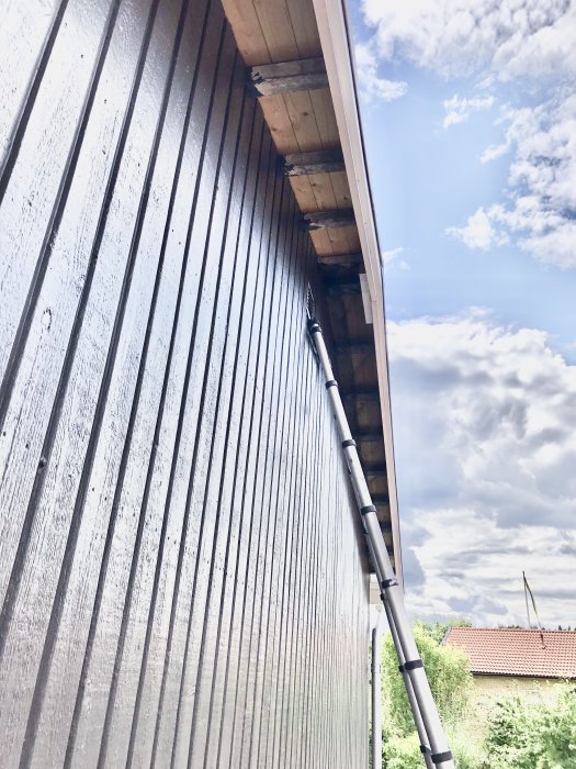 Renoverad takfot på hus med lång bräda som stöds av stege mot klar himmel.