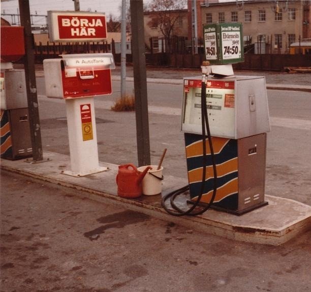 Gammal bensinmack med sedelautomat, bensinpump och röd kanna, i ett öde gatumiljö.