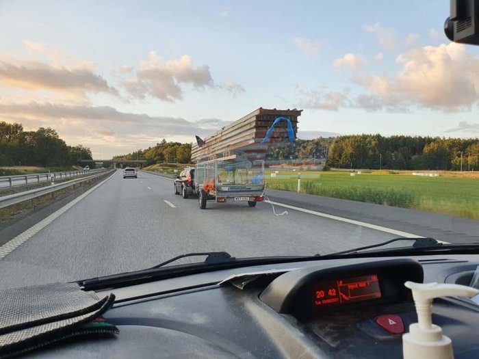 Överlastad släpvagn med snedställda och utstickande byggmaterial på motorväg.