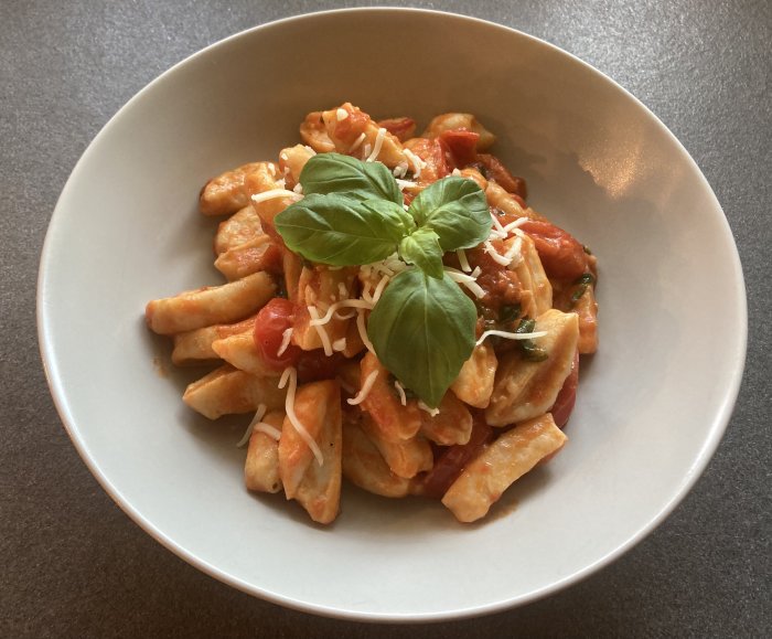 En tallrik med pasta toppad med tomatsås, riven ost och ett basilikablad.