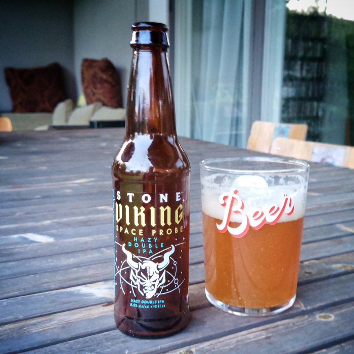 En ölflaska och ett ölglas på ett trädgårdsbord, med texten "Viking Space Probe Hazy Double IPA".