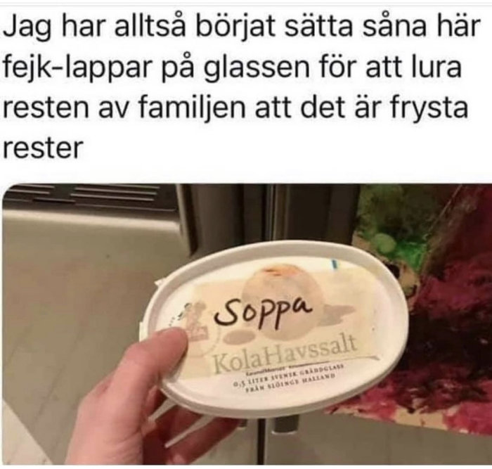 Hand håller ett glasslock med fejklapp märkt "Soppa KolaHavssalt" som ett skämt för att lura familjen.