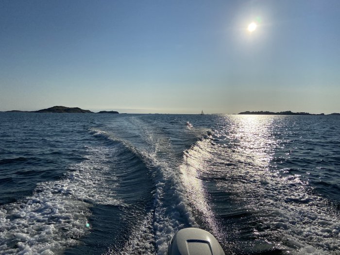 Utsikt från en båt som färdas på havet, med kölvatten och solreflexion på vattnet, mot bakgrund av öar.