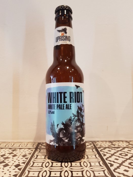 Flaska av 'Uprising White Riot' pale ale på en mönstrad yta.