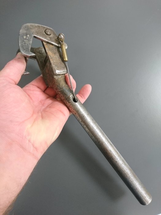 Hand håller ett metallverktyg med två leder och stansad fjäderfästanordning, märkt med "PAT".