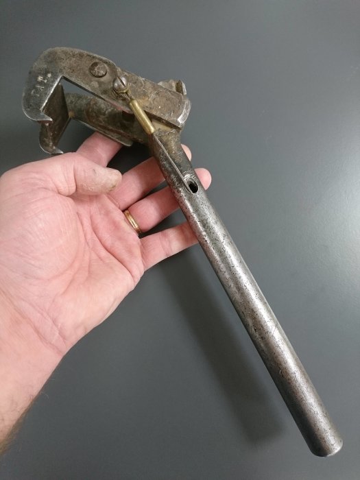 En hand håller ett gammalt, ledat verktyg med texten "PAT" utan synliga siffror.