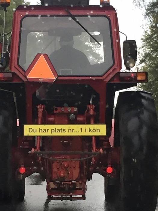 Bakifrån syn på en röd traktor i regn med en skylt som läser "Du har plats nr...1 i kön