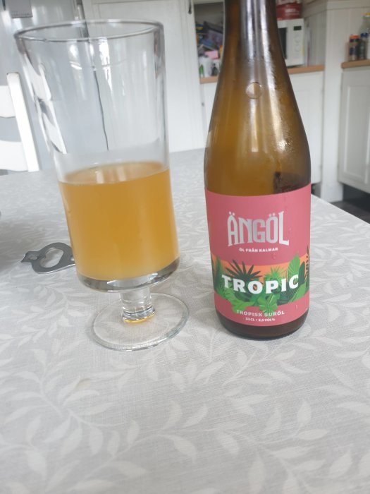 En delvis drucken suröl i glas bredvid en flaska med etiketten "TROPIC" på ett mönstrat bord.