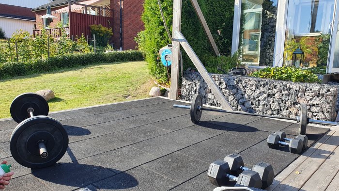 Utomhus träningsplats med skivstång, hantlar och gummiplattor på en terrass.