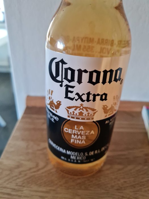 Flaska av Corona Extra öl står på ett bord, halvtom med fokus på etiketten.