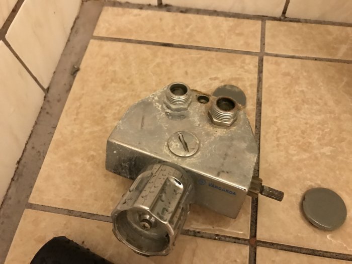 Gamla blandare på kakelvägg med skada, avsedd för reparation eller byte.