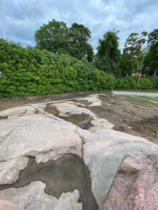 Ojämnt berg med två utlagda reglar som markerar framtida växthusplats på en stadstomt.