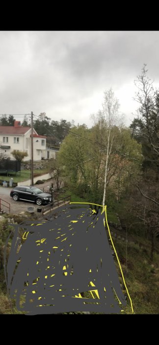 Utsikt över liten parkeringsplats med bil, markerad framtida utbyggnad på en slänt med gula skisser.