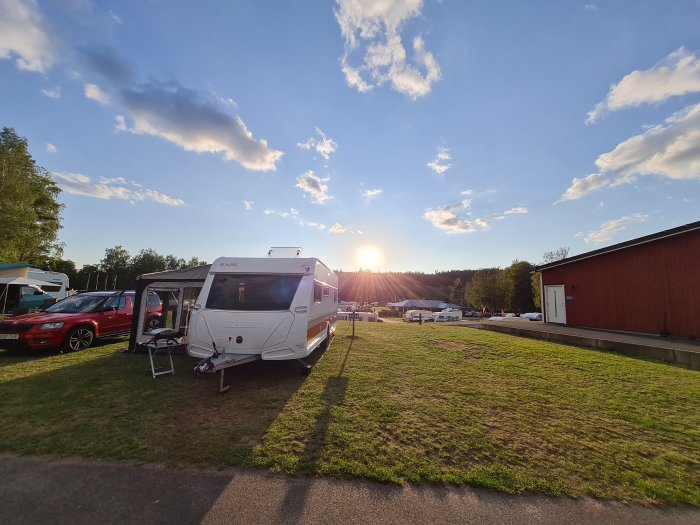 Husvagn på campingplats med öppen förtält vid solnedgång, omgiven av andra fordon och grönt gräs.