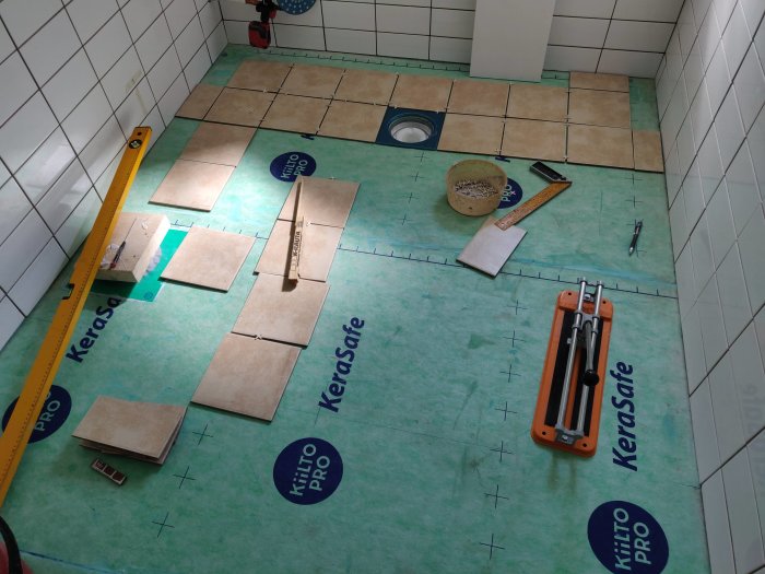 Uppmätt badrumsgolv inför klinkerläggning med kakelplattor, verktyg och snörslå.