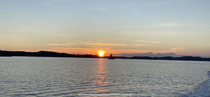 Solnedgång över vattnet med silhuett av ett skepp mot den glödande himlen.