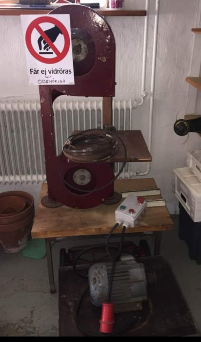 Begagnad röd bandsåg på arbetsbänk med varningsskylt och strömbrytare.