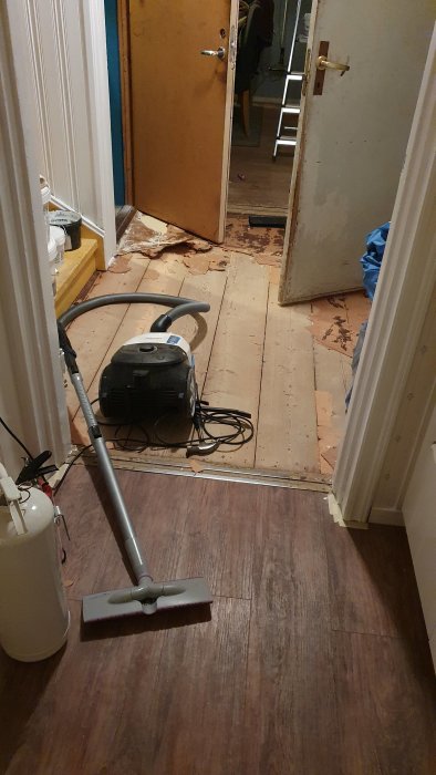 Golvrenovering pågår med dammsugare, delvis borttaget golv och tröskel.