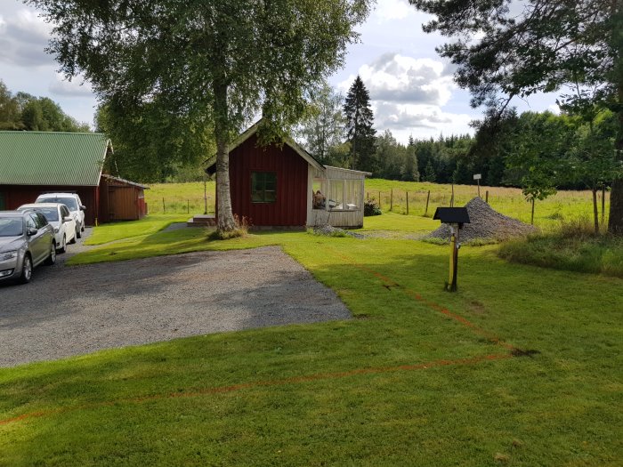 Gräsmatta med uppmärkta linjer för utvidgning av parkering och en hög med bergkross i bakgrunden.