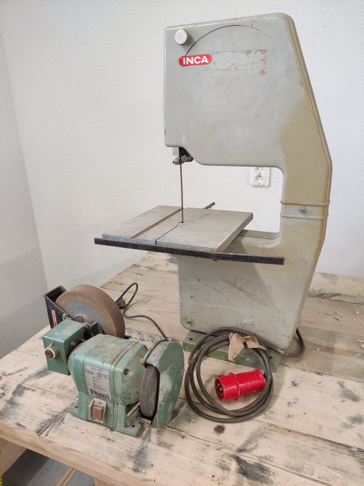 En bandsåg och en bänkslip med tecken på rost, ej använda på ett tag, ligger på ett arbetsbord.