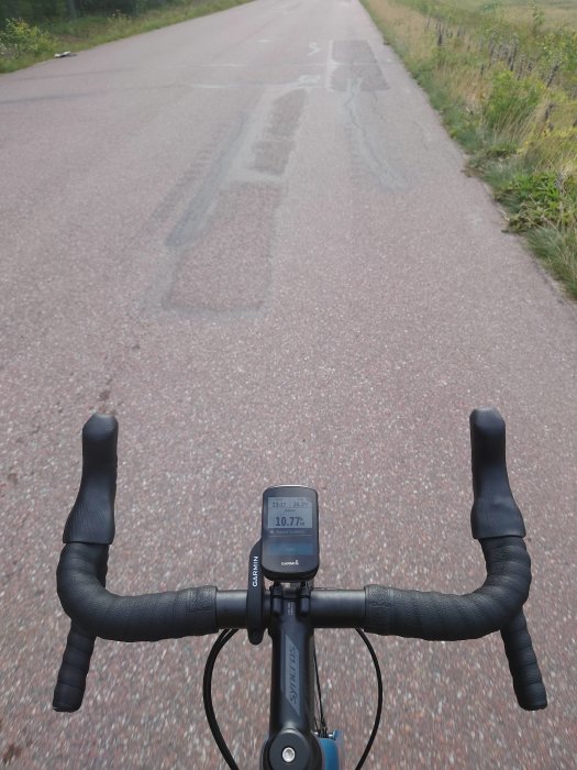 Cyklistperspektiv på en landsväg med cykelstyret och cykeldator synligt i förgrunden.