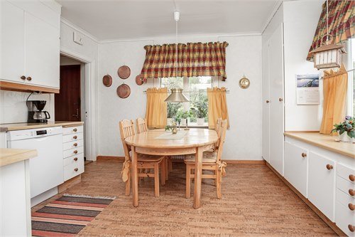 Ett traditionellt kök med matbord, stolar, vita skåp och kopparredskap på väggen.