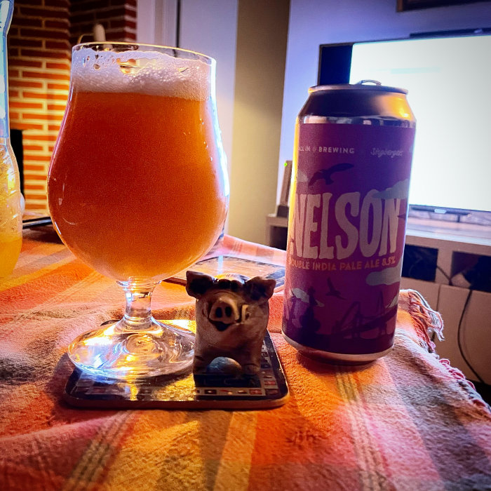 Ett glas öl på ett underlägg med en liten grisfigur framför och en ölburk bredvid på ett bord.