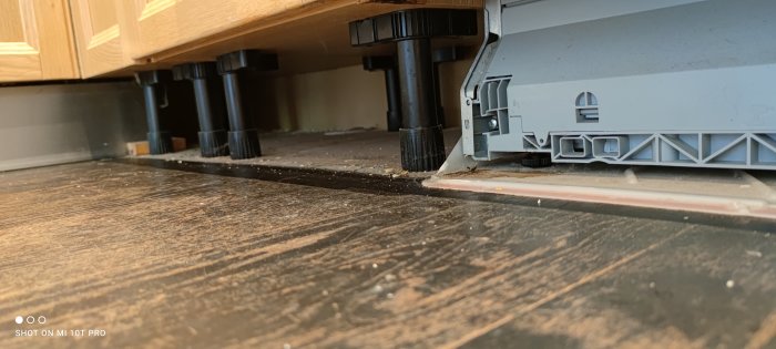 Vy under köksskåp som visar detaljer av befintligt golv och justerbara skåpbensstöd.