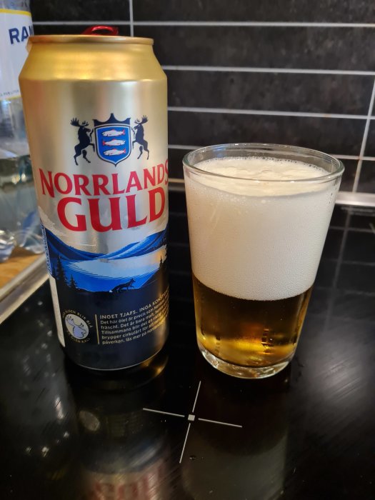 Ölburk och ett glas med Norrlands Guld på ett svart bänkskiva, som firande under semestern.