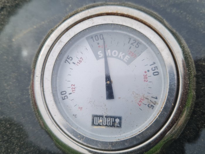 Termometer på en smoker visar ca 107 grader Celsius, indikerar pågående grillning.