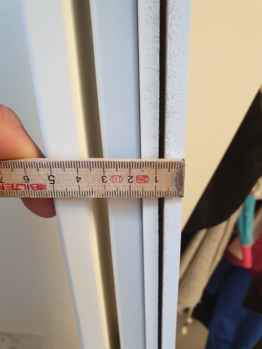 Måttstock som visar ett avstånd på en vit fönsterkarm med två olika bredder på tapparna.