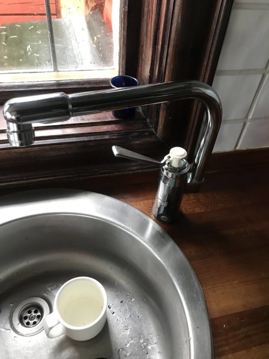 Köksblandare med delvis demonterad insats vid diskho, verktyg syns och kopp i ho.